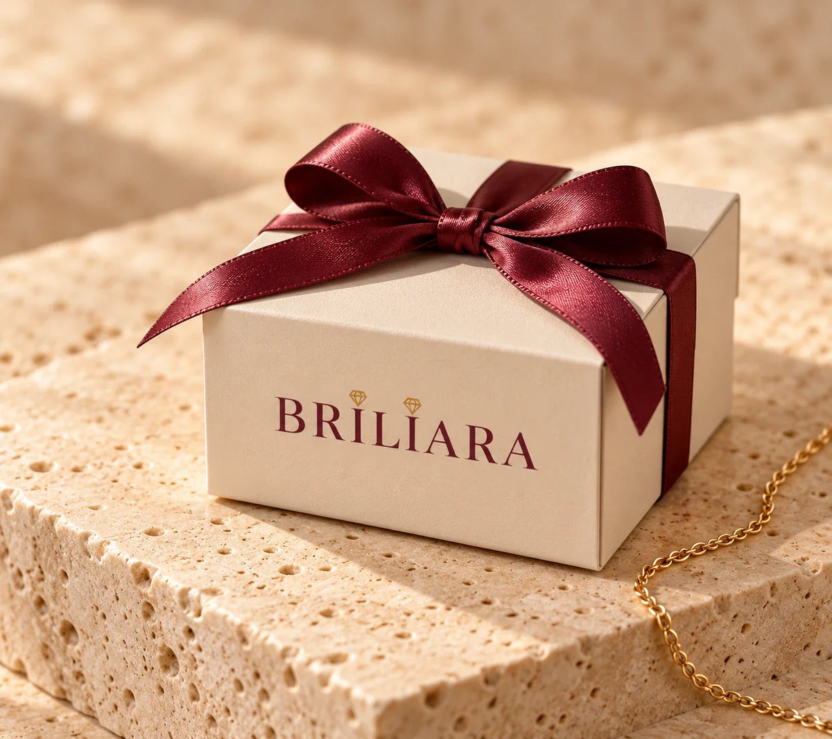 Caja de regalo BRILIARA color marfil con lazo burdeos sobre piedra beige